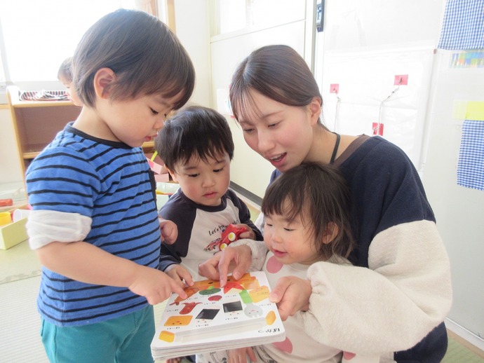 1歳児が保育者と絵本を見ている写真