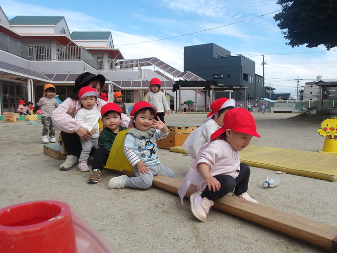 写真：1歳児が平均台の上に並んで座っている